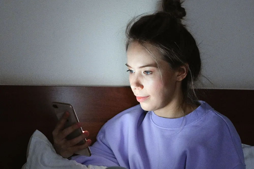 Karanlık odada yatağında oturup telefon ekranına bakan genç bir kadın